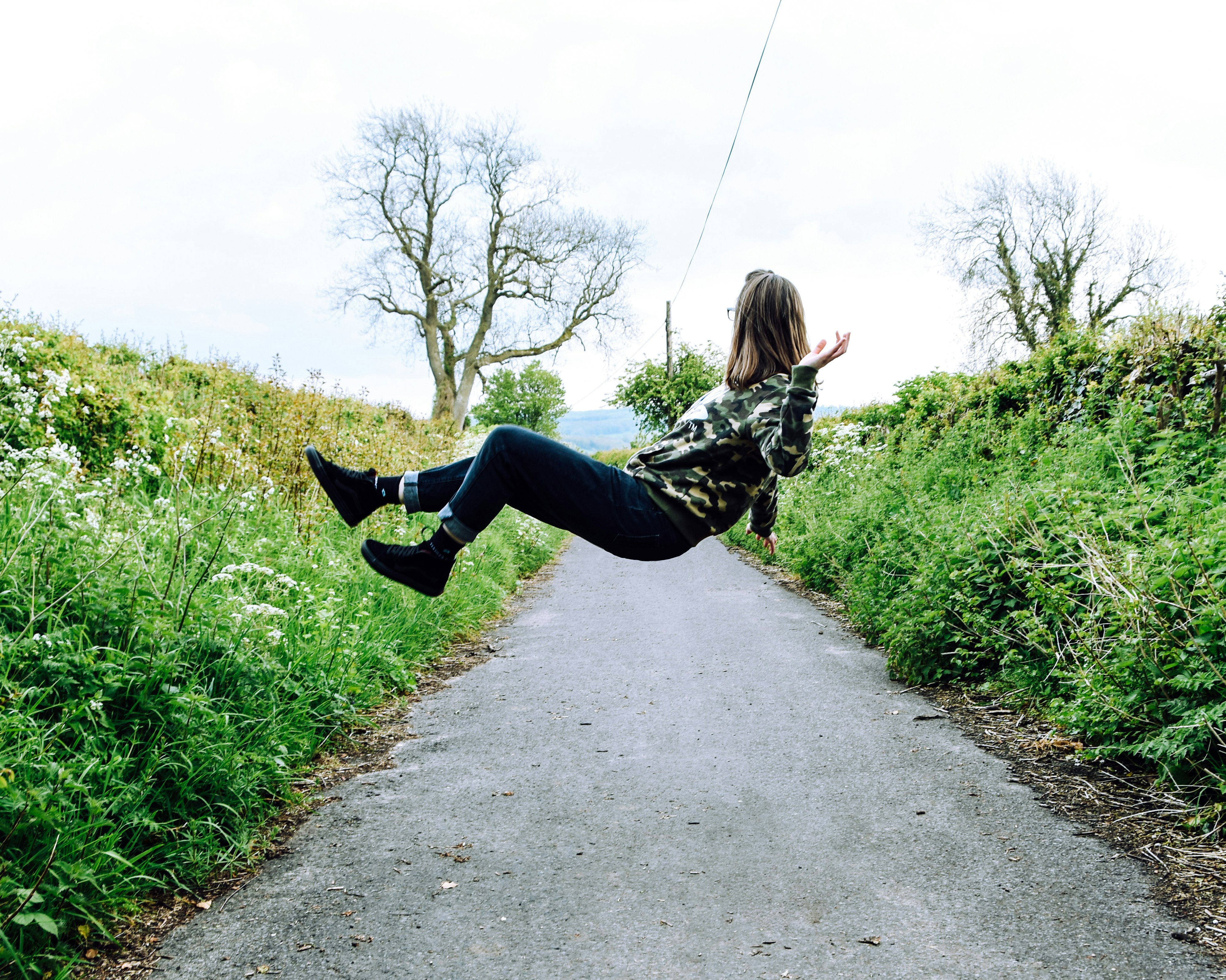 girl in hoodie and blue denim jeans levitating on gray concrete lane during daytime